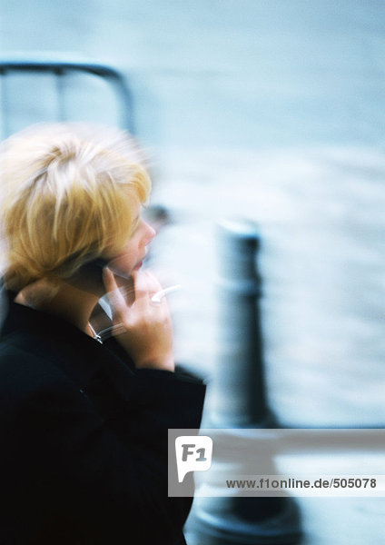Woman holding cell phone in street  blurred