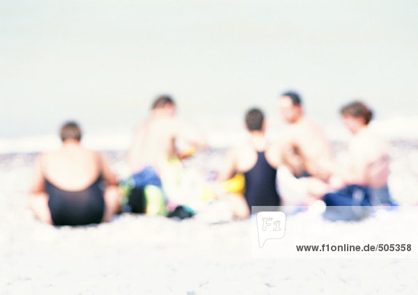 Gruppe von Menschen  die auf Sand am Strand sitzen  verschwommen