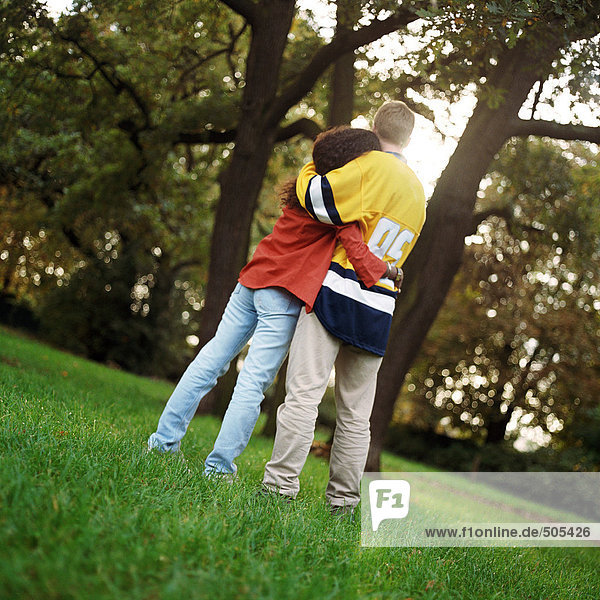 Young man and woman standing on grass  embracing  rear view  full length