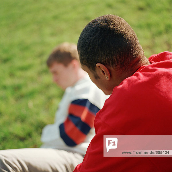 Zwei junge Männer  einer sitzt auf Gras.