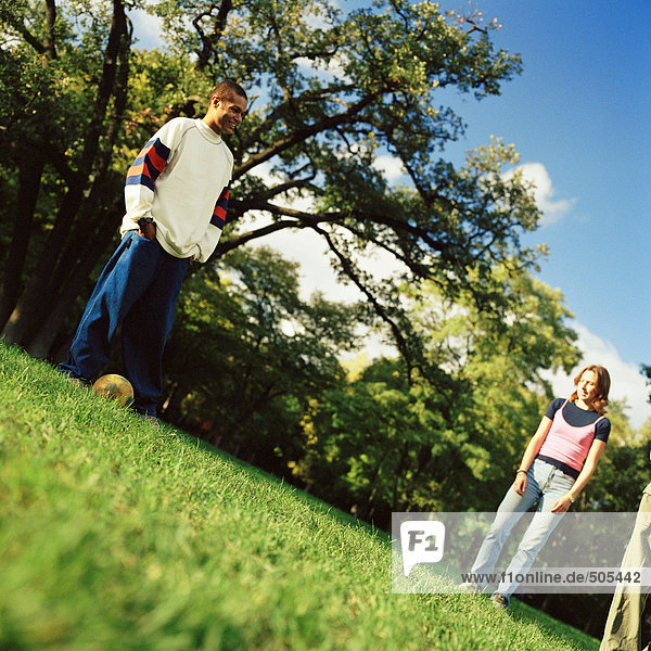 Junger Mann auf Rasen stehend mit Fußball,  junge Frau schaut ihn an,  niedriger Blickwinkel