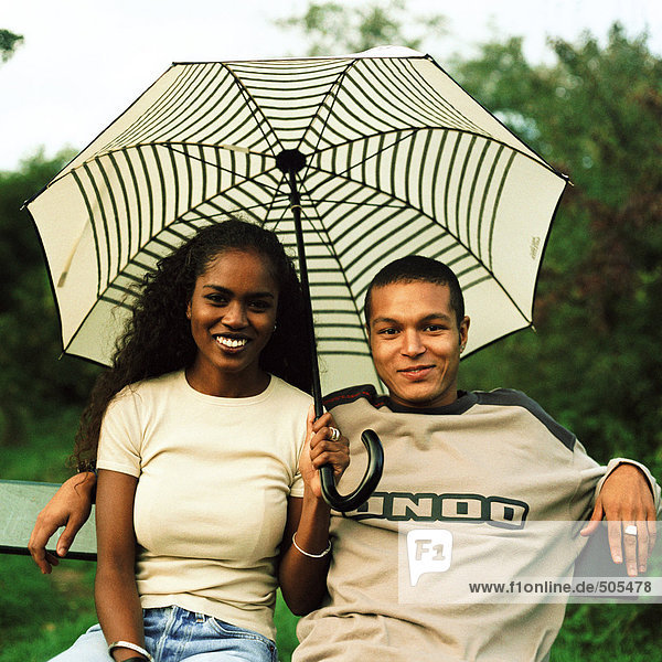 Junger Mann und junge Frau lächelnd und sitzend unter dem Regenschirm im Freien