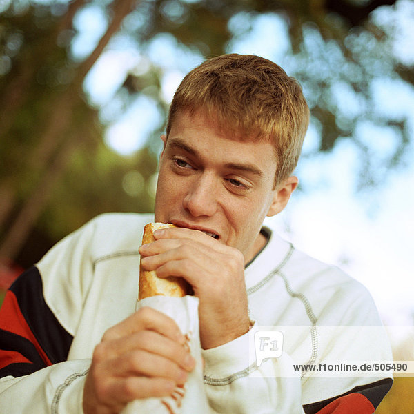 Junger Mann isst Sandwich draußen