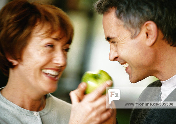 Man and woman smiling at each other  holding apple between them  close up  blurred