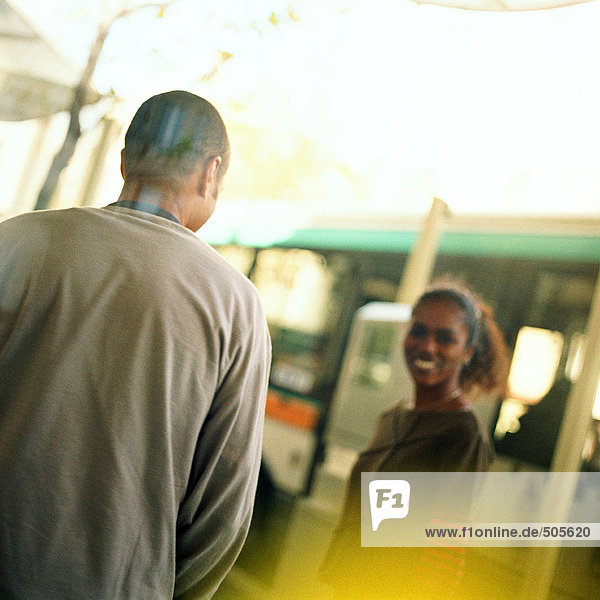 Junger Mann und junge Frau am Busbahnhof  draußen.