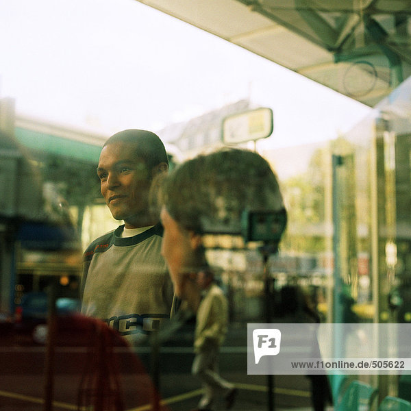 Junge Leute durchs Fenster mit Reflexionen gesehen  draußen am Busbahnhof