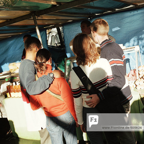 Junge Paare mit Armen umeinander  auf dem Straßenmarkt stehend  Rückansicht