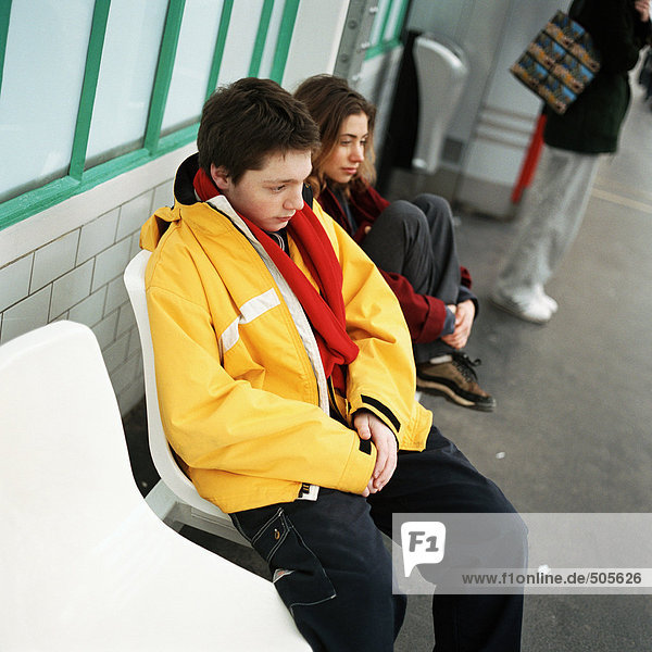Junger Mann und junge Frau sitzen nebeneinander auf dem Bahnsteig der U-Bahn  draussen