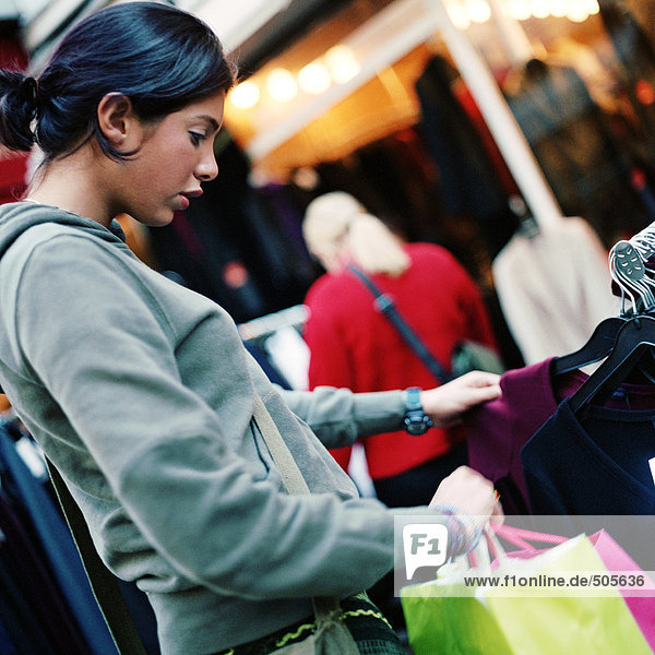Teenagermädchen schaut auf Kleiderständer  hält Einkaufstaschen  draußen