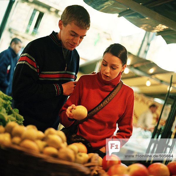 Young couple looking at fruit at outdoor market  fruit blurred in foreground