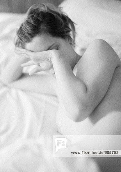 Nackte Frau auf dem Bett liegend  berührendes Gesicht mit Handrücken  schwarz-weiß.