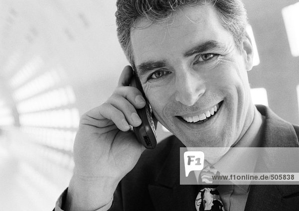 Businessman talking on cellular phone smiling at camera  close-up.