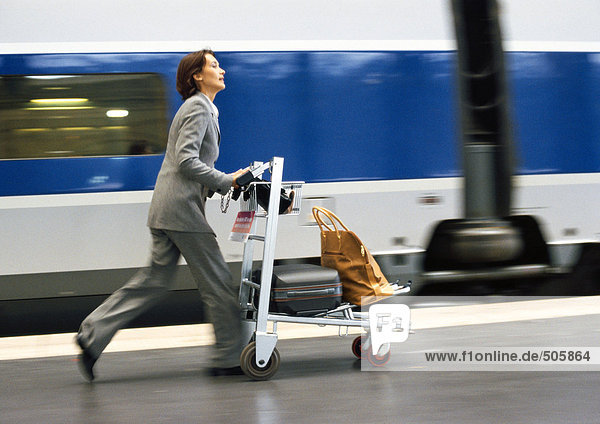 Geschäftsfrau hetzt mit Wagen und Gepäck auf dem Bahnsteig  neben dem Zug  verschwommen.