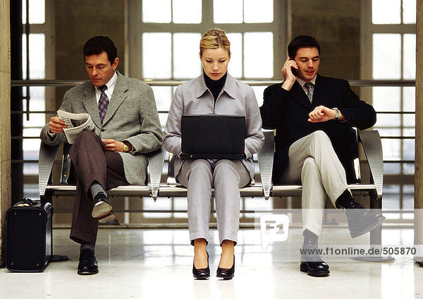 Businesswoman using laptop sitting between two businessmen.