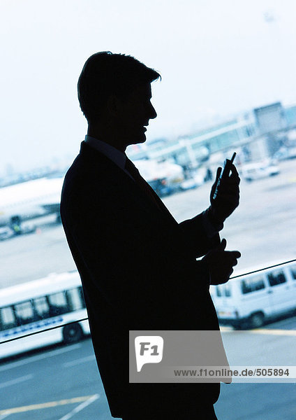 Geschäftsmann schaut auf Handy im Flughafen  Silhouette.