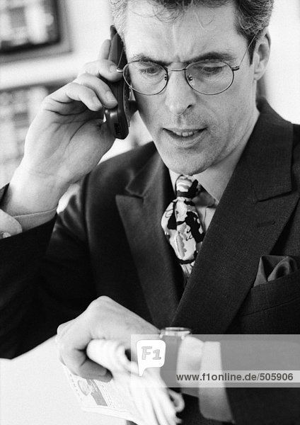 Businessman talking on cellular phone  checking time  head and shoulders  b&w.