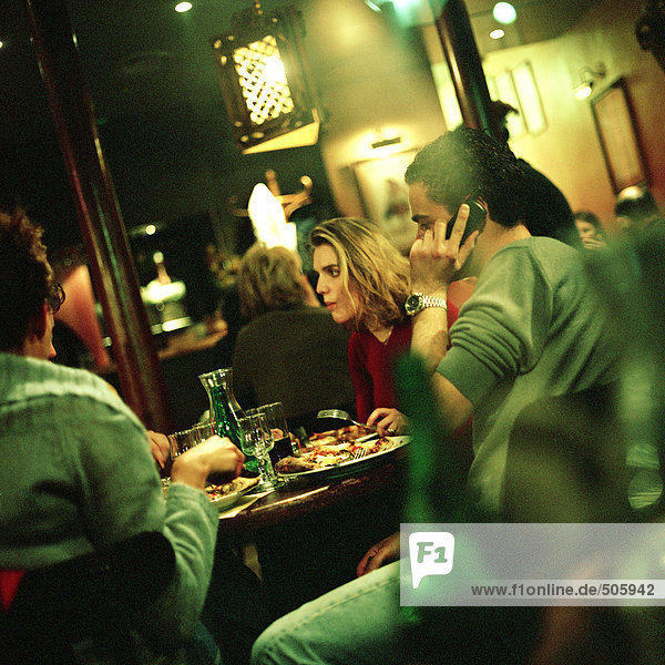 Gruppe junger Leute  die am Tisch im Restaurant essen  ein Mann mit dem Handy.