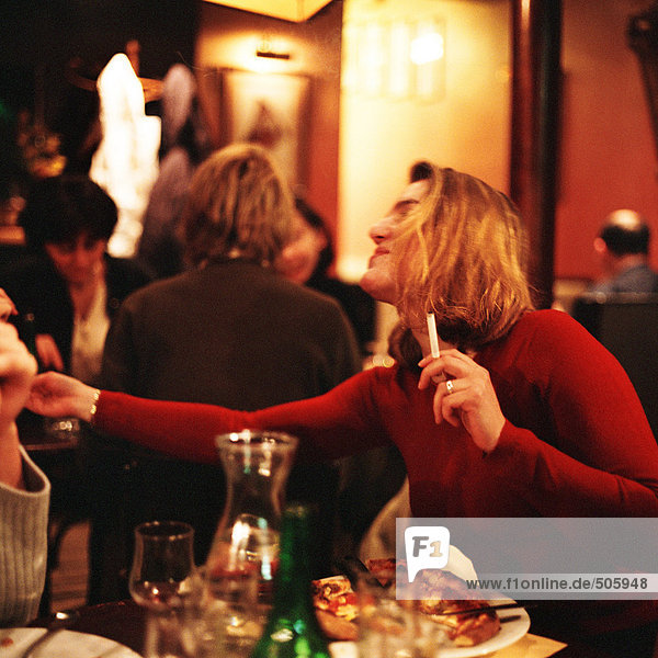Frau sitzt am Tisch im Restaurant  raucht eine Zigarette und erreicht