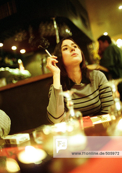 Eine junge Frau sitzt im Café und raucht eine Zigarette.