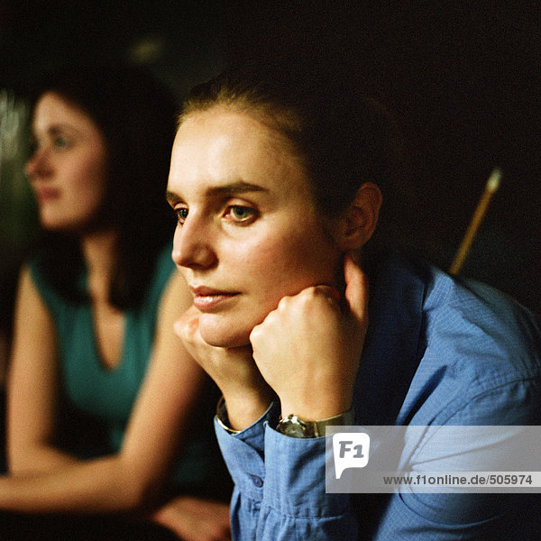Junge Frau ruht Kopf auf Händen  Porträt  zweite junge Frau im Hintergrund sitzend