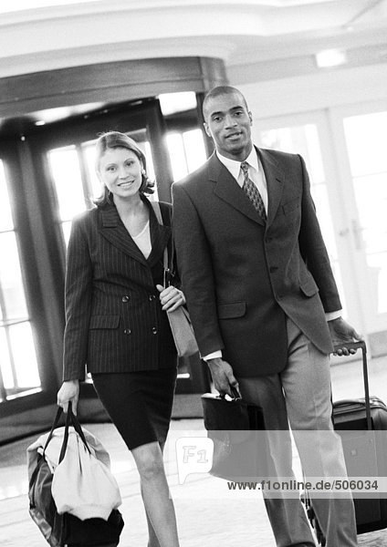 Geschäftsmann und Geschäftsfrau gehen zusammen im Gebäude mit Gepäck  s/w.