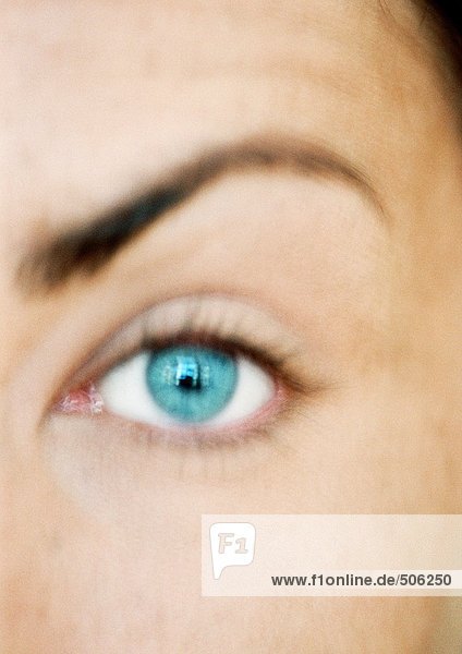 Blaues Auge und erhabene Augenbraue der Frau  Blick in die Kamera  Nahaufnahme  verschwommen.