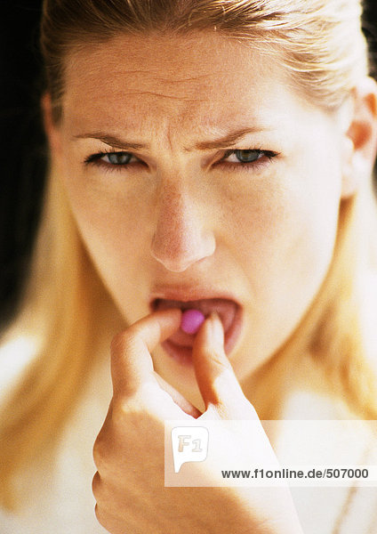 Eine Frau steckt die Pille in den Mund  schaut in die Kamera.