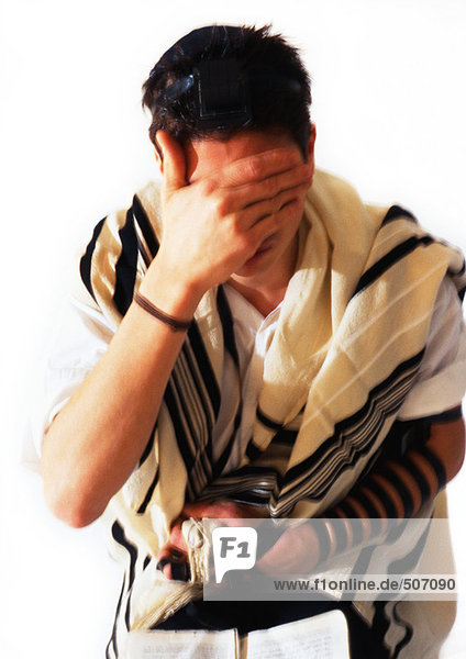 Jewish man wearing Tefillin and Tallith for prayer  covering face with hand  close-up