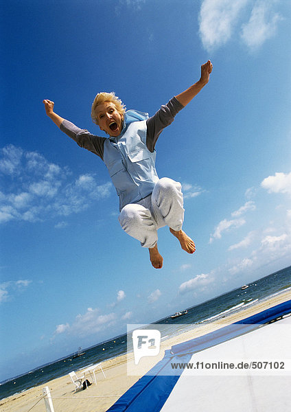 Mature woman jumping on trampoline at beach