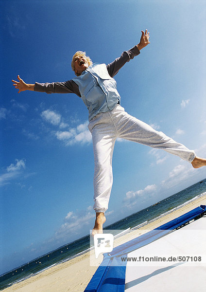 Mature woman jumping on trampoline at the beach  low angle view
