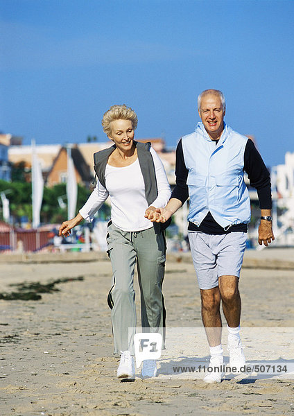 Mature couple holding hands walking on beach  front view  full length