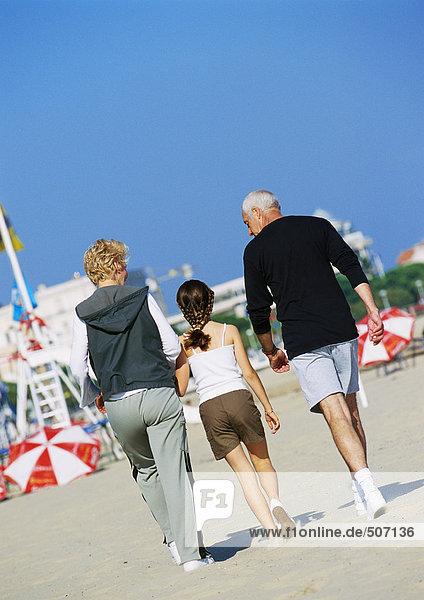 Mature couple walking with girl on the beach  rear view  full length