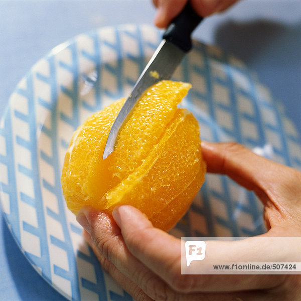 Nahaufnahme der Hände  die mit einem Messer geschältes Orange schneiden.