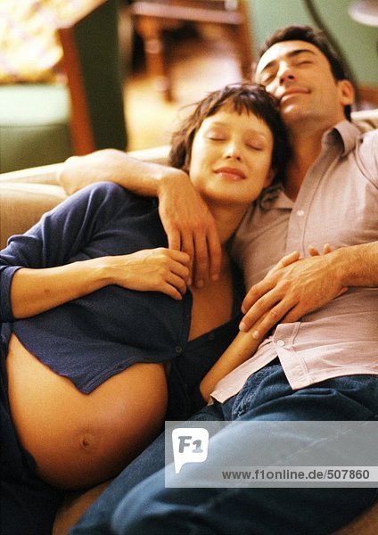 Pregnant woman and man lying on sofa  smiling