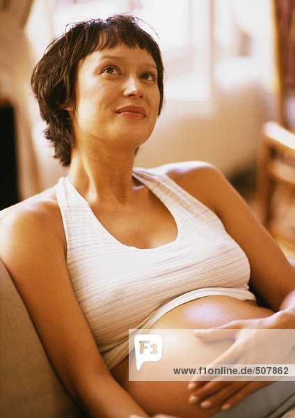 Pregnant woman in armchair  hand on belly and looking up