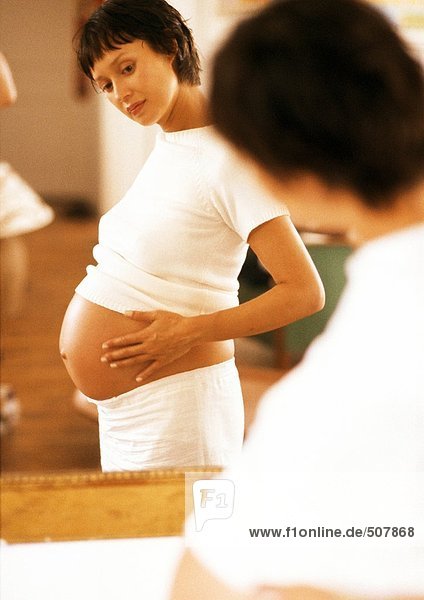 Schwangere Frau schaut auf ihren Bauch im Spiegel