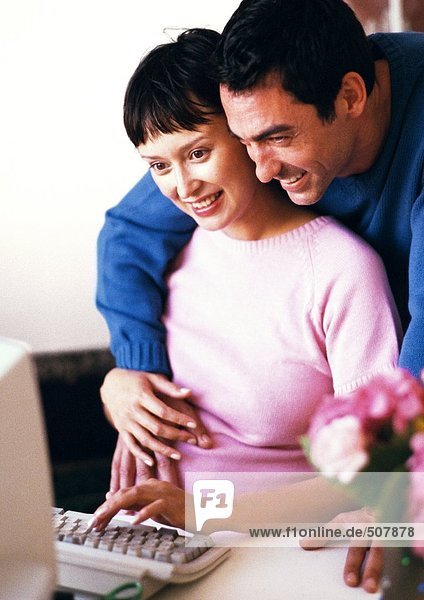 Pregnant woman using computer  man with arms around her looking over her shoulder