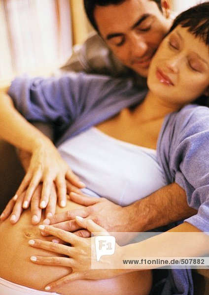Mann berührt den Bauch einer schwangeren Frau von hinten