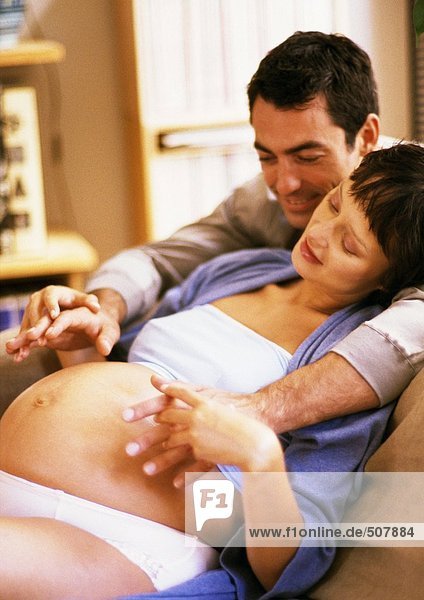 Mann  der auf den Bauch einer schwangeren Frau schaut und ihre Hände hält.