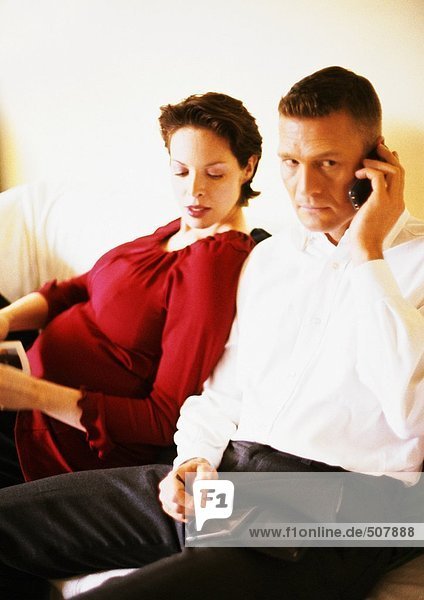 Pregnant woman sitting with man using cell phone