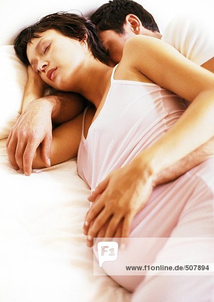Mann umarmt schwangere Frau im Bett