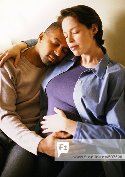 Pregnant woman sitting with arm around man  portrait