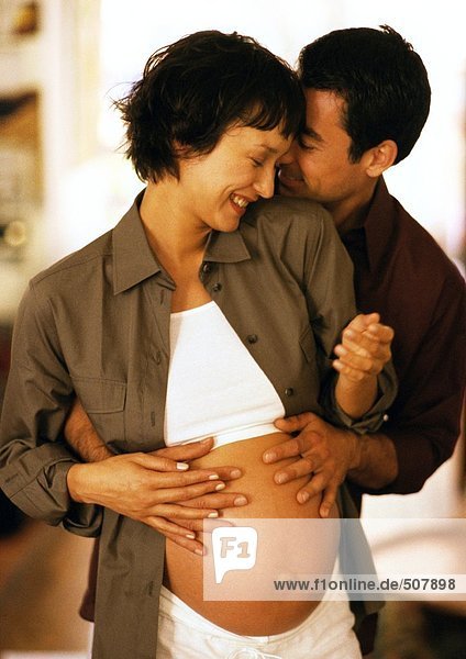 Mann berührt den Bauch einer schwangeren Frau von hinten