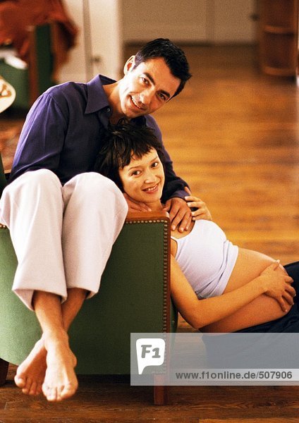 Man sitting backwards on chair and pregnant woman sitting on floor  leaning head on man  portrait
