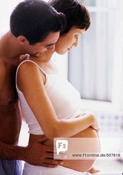 Man holding pregnant woman's waist and looking over her shoulder  side view
