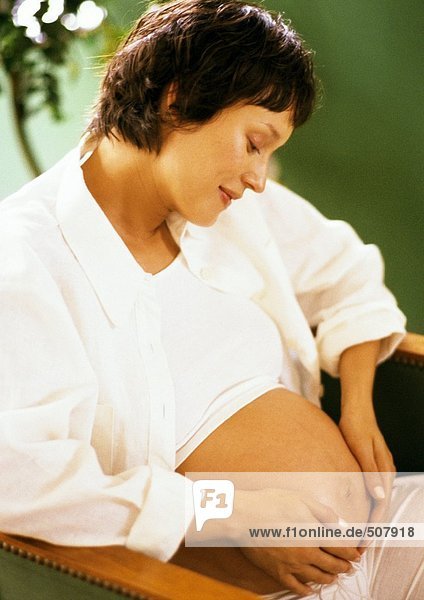 Schwangere Frau mit Händen auf dem Bauch  Blick nach unten
