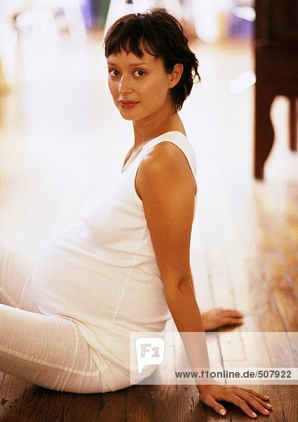 Schwangere Frau sitzt auf dem Boden  schaut in die Kamera  Seitenansicht  Porträt