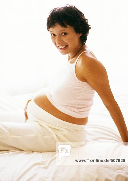 Pregnant woman sitting on bed  smiling at camera  portrait
