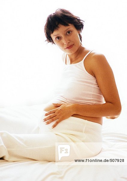 Pregnant woman sitting with hand on stomach  looking at camera  portrait