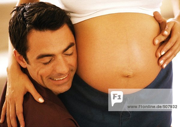Man pressing cheek to pregnant woman's stomach  close-up